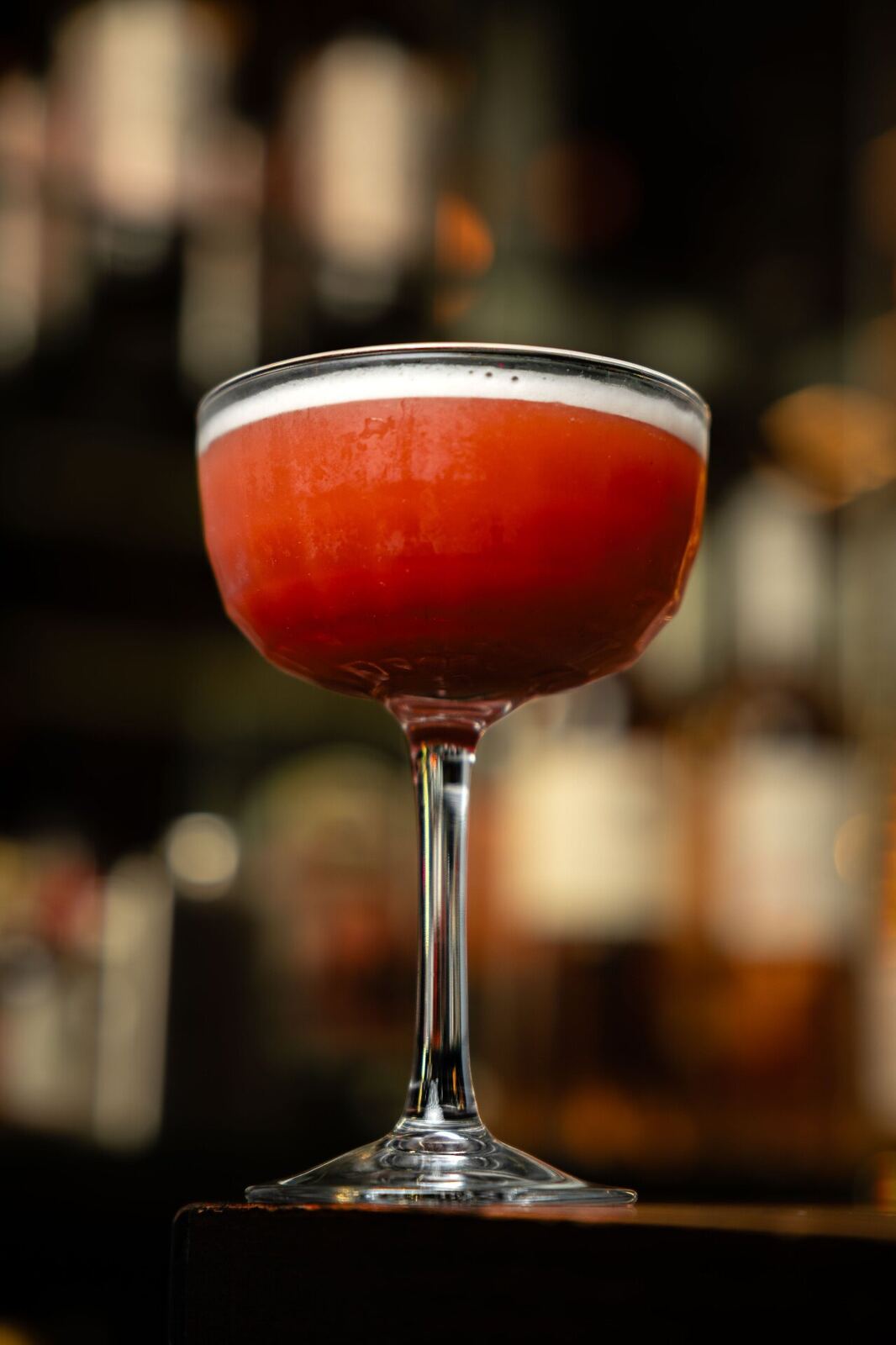 Coupe con cocktail rosso e backbar sfocato